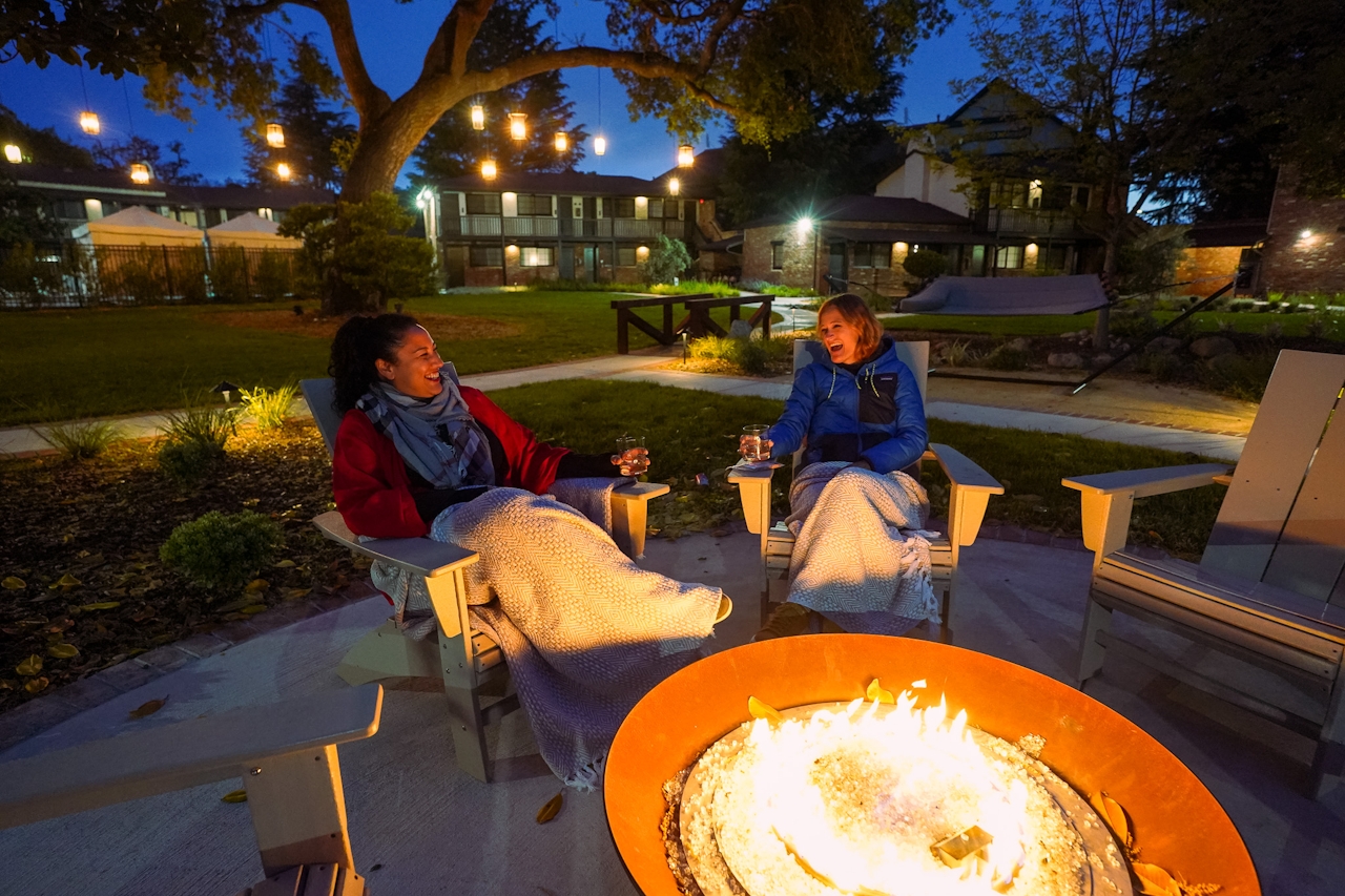Two women sit around a firepit in the back garden and lawn area of the Paso Robles Inn