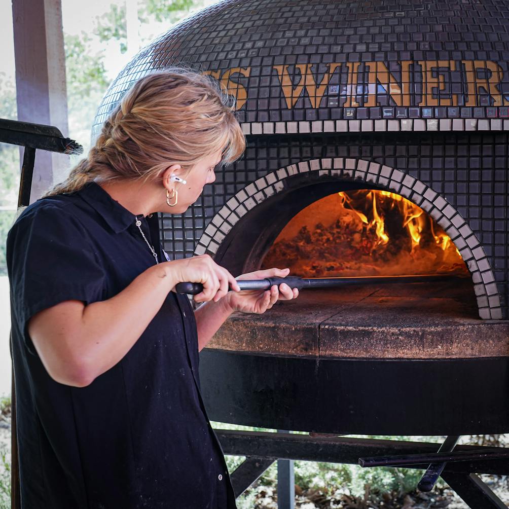 A woman manages the woodfire pizza oven on the patio Cass Vineyard and Winery near Paso Robles