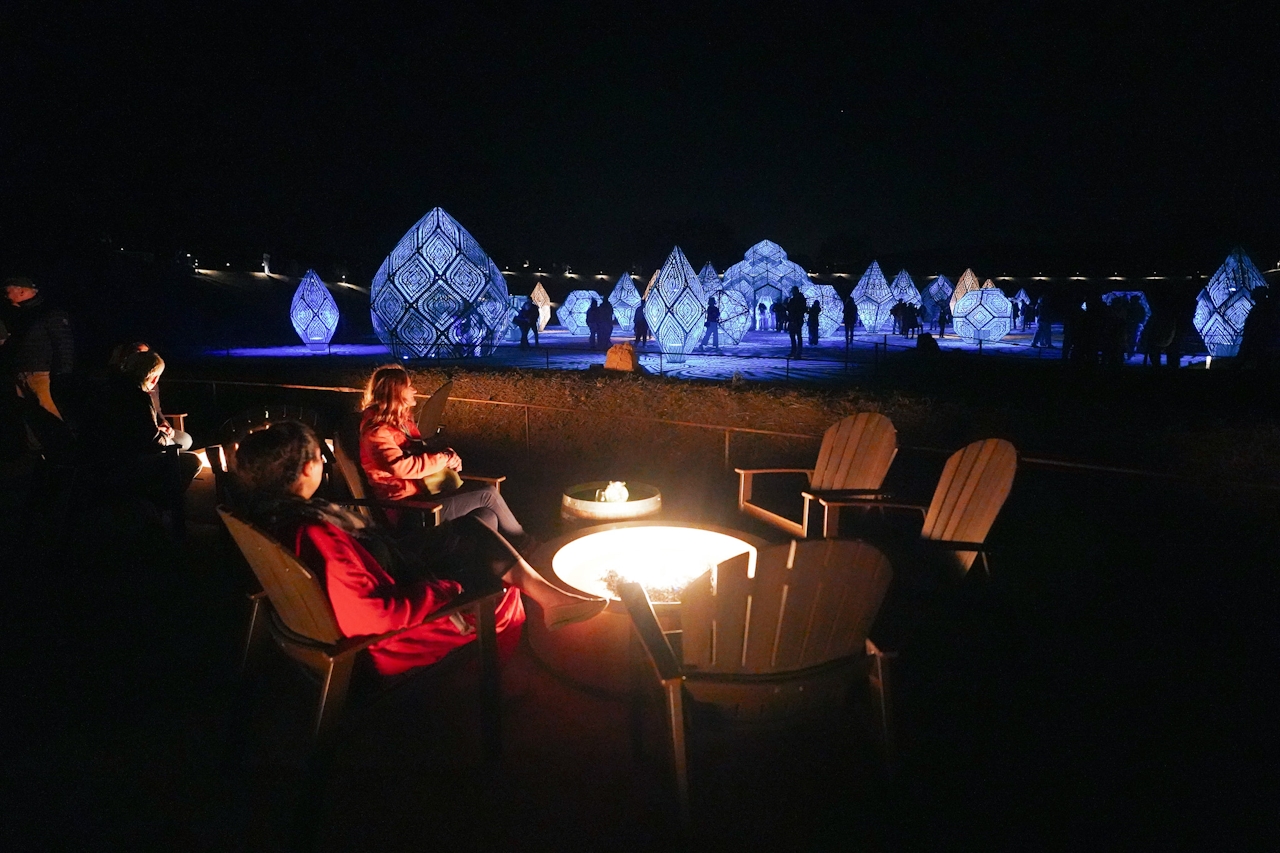 People sit in front of a firepit while looking out at the colorful Dimensions exhibit at Sensorio light exhibition in Paso Robles 