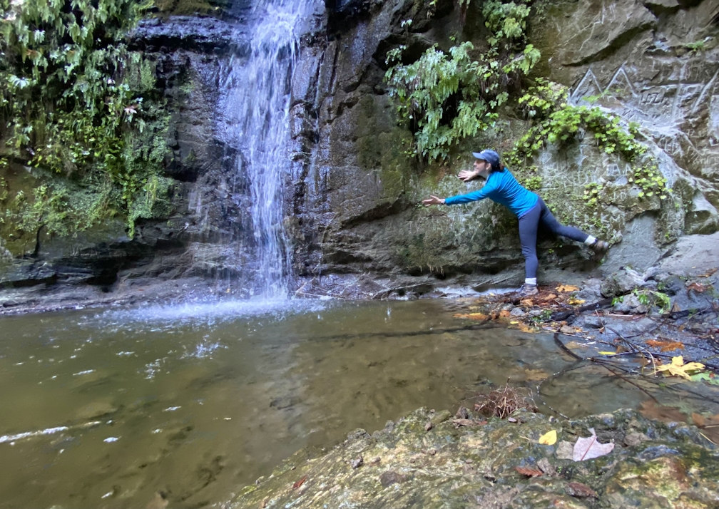 Woman hiking reaching out towards Maple Falls in The Forest of Nisene Marks State Park