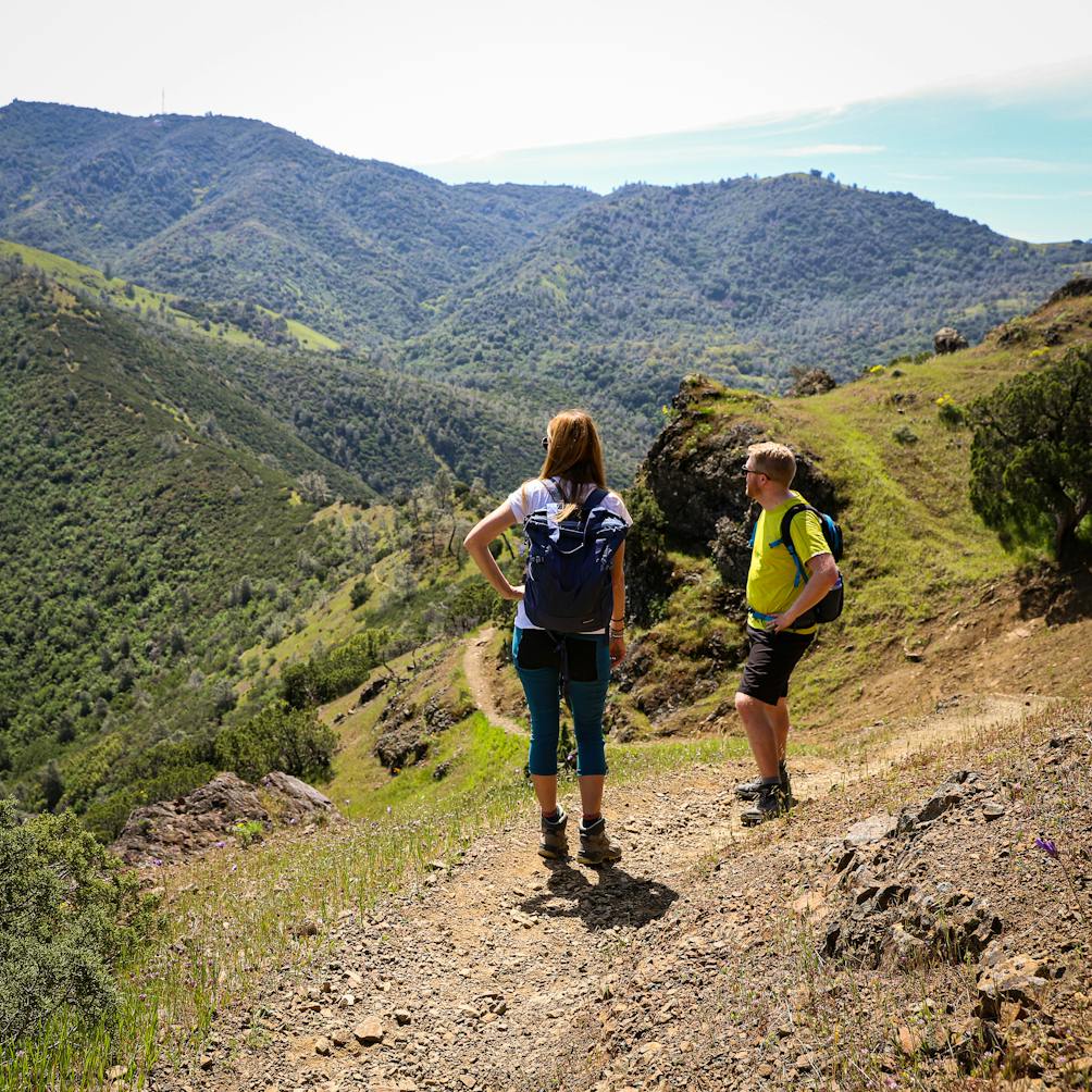 Two hikers are taking in the view of mountains and green rolling hills on a trail at Mount Diablo State Park