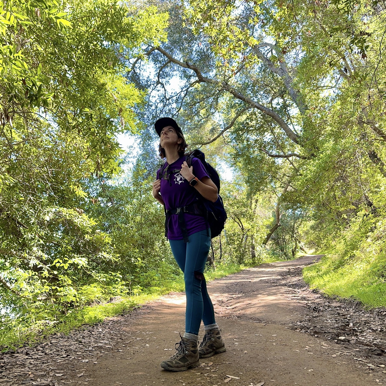 Hiker standing amid green trees on the Sendador Mine Trail in Almaden Quicksilver County Park